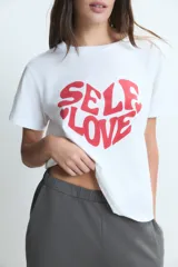 Remera blanca de algodón con estampa frontal en color rojo que forma un corazón con la frase 'Self Love'.