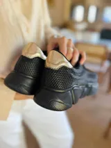 Championes urbanos de mujer con diseño de malla texturizada en color negro y detalle metálico en tono dorado en el talón. Poseen una suela gruesa y resistente, ideal para uso diario.