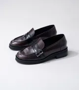Mocasín de cuero vacuno negro con detalle de pieza de cuero con textura de cocodrilo y hebillas metálicas. Suela de caucho con plataforma.