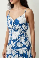 Vestido corto sin mangas, con escote en V y tirantes finos ajustables. Presenta un diseño estampado en tonos azul y blanco con motivos florales, cintura elástica fruncida y falda con vuelo y detalle de volados.