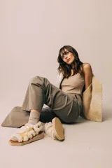 Sandalias de diseño moderno con tiras de cuero metalizado en color dorado, bordeadas con corderito sintético blanco. Poseen una suela plana con plataforma geométrica y cierre con hebilla lateral.