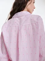 Camisa de dormir de popelina de algodón, con estampado de rayas verticales y pequeños motivos geométricos. Presenta cuello camisero, mangas largas y cierre frontal mediante lazos ajustables.