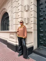 Camisa de color marrón chocolate con cuello redondo grande y ribetes en color amarillo vibrante. Presenta cierre frontal con botones amarillos, mangas largas con puños elásticos y un corte holgado.