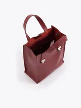 Cartera tipo tote pequeña de cuero color tostado, con doble asa superior y herrajes metálicos plateados en forma de llama en la base de las manijas. Presenta el logo de la marca estampado en la parte inferior frontal.