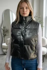 Chaleco puffer de efecto engomado en color negro, con cuello alto y cierre frontal mediante botones a presión. Presenta un diseño acolchado con costuras horizontales y bolsillos laterales.