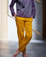 Pantalón babucha color beige de algodón, con corte a la cintura y piernas levemente amplias. Presenta textura de tablitas centrales y elásticos con broches inferiores que ajustan las piernas al tobillo.