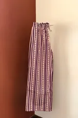 Pantalón de corte recto y holgado con cintura elástica ajustable mediante cordón. Presenta un diseño de rayas verticales en tonos rosa y violeta, decorado con una pequeña estampa repetitiva de flores rojas a lo largo de cada franja clara.