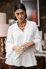 Blusa blanca de textura arrugada, con cuello alto, abertura frontal tipo gota y mangas largas acampanadas con detalle de frunces.