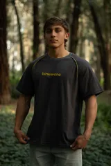 Remera gris oscuro de manga corta raglán, confeccionada en algodón. Presenta costuras a la vista en color amarillo.