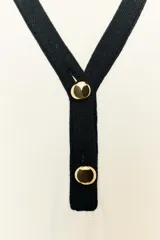 Vestido corto de tejido suave, color negro con detalles en blanco. Presenta cuello solapa, escote en pico, manga larga, falsos bolsillos delanteros y cierre frontal con botones dorados.