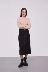 Falda midi de jean color negro, de tiro alto y corte recto. Presenta costuras a la vista en color ocre y cierre frontal con botón y cremallera.