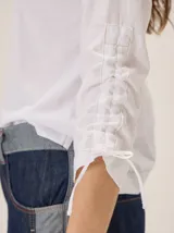 Remera de manga larga color blanco con cuello redondo y detalles fruncidos con lazos en las mangas.
