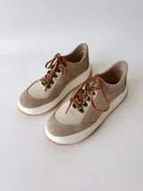 Championes de cuero color visón con cordones marrones, suela blanca y base color caramelo.