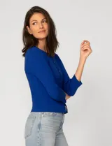 Cardigan blanco de tejido liviano con trama en relieve, cuello a la base y cierre frontal con botones a tono. Presenta mangas tres cuartos.