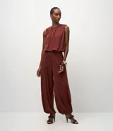 Pantalón estilo aladino de tiro alto con cintura elástica ancha y puños elásticos en los tobillos. Confeccionado en tejido de poliéster con un acabado levemente brillante y caída fluida.