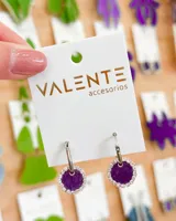 Aros colgantes con aro de acero plateado y dije circular forrado en tela color violeta con borde de strass plateado.