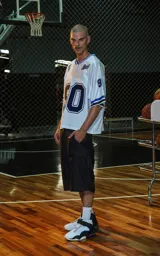 Camiseta estilo jersey de fútbol americano, color blanco, con cuello en V ribeteado en azul. Presenta el número "90" grande en el frente en azul marino con borde blanco. Tiene bordados en el pecho como "Lx." y "Ravers", y números pequeños en las mangas. Los puños tienen franjas azules y negras.