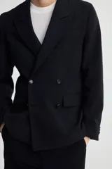 Blazer negro de doble botonadura con solapas de pico, bolsillo superior, bolsillos delanteros ribeteados con solapa, tres bolsillos interiores, botones decorativos en los puños y abertura doble atrás.