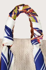 Pañuelo cuadrado con estampado floral y geométrico central en tonos naranja, amarillo, verde y azul, enmarcado por un borde azul marino con líneas blancas. Presenta un acabado sedoso.