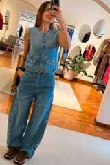 Chaleco de denim sin mangas, con cierre frontal de botones y bolsillos delanteros decorados con tachas metálicas.