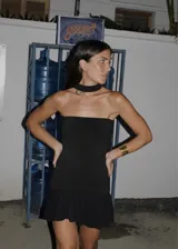 Vestido corto negro de tejido de punto, con diseño strapless y cuello tipo choker integrado. Presenta un corte ajustado al cuerpo en el torso y una falda con vuelo y tablitas en el ruedo.