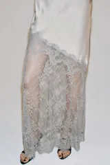 Vestido largo de satén y encaje color gris, con cuello redondo, manga larga y cierre en la espalda con abertura y botón.