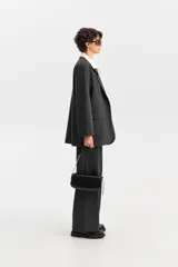 Blazer de corte amplio en color gris oscuro, con solapas de muesca y bolsillos de ojal. La prenda simula llevar una camisa blanca de cuello ancho por debajo, con los botones visibles en el frente.