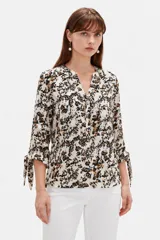 Blusa estampada de viscosa con diseño abstracto en tonos beige, negro y marrón, escote en V con cuello mao y mangas tres cuartos con detalles de lazos en los puños.