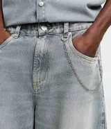 Pantalón de jean estilo baggy balloon, de corte holgado con volumen en las piernas y cintura fija con trabillas. Presenta costuras a contratono y detalle de cadena metálica lateral.