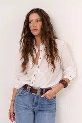Camisa de manga larga color blanco, con cuello clásico, cierre frontal con botones marrones y costuras pespunteadas en contraste.
