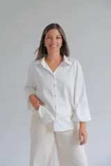 Camisa blanca de corte holgado con cuello clásico, cierre frontal de botones y mangas tres cuartos con sutil detalle bordado en los puños.