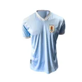 Camiseta de fútbol celeste con cuello en V y mangas cortas con ribete blanco. Escudo de Uruguay bordado en el pecho.