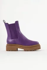 Bota tipo chelsea con suela track de goma en color marrón y capellada de cuero negro. Presenta elásticos laterales y tirador trasero.