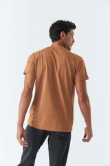 Remera color marrón con cuello redondo y manga corta. Presenta un estampado vertical con texto en japonés y líneas onduladas. Corte recto.