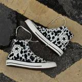 Championes Converse modelo Chuck Taylor All Star Hi, con diseño de estampado animal print de manchas negras sobre fondo crema. Presentan puntera de goma, cordones blancos y suela de goma vulcanizada con detalles en negro.