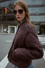 Chaqueta acolchada de cuello redondo y manga larga, con cierre frontal de botones y dos bolsillos delanteros de plastrón. Presenta un diseño de costuras en forma de rombos.