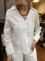Camisa blanca con escote en V y cuello camisero, de manga larga con puños anchos y cierre frontal de botones.