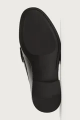 Mocasines de vestir tipo loafer para hombre, confeccionados en cuero marrón oscuro con acabado brillante. Presentan diseño clásico de antifaz en el empeine, costuras visibles en relieve y suela plana con un ligero tacón.