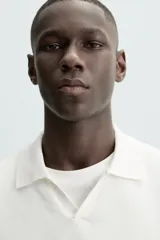 Jersey de punto color verde oliva, de calce relajado (relaxed fit), con cuello solapa y abertura frontal en forma de V. Es de manga corta y presenta acabados en rib en puños y ruedo.