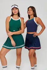 Conjunto deportivo de dos piezas color verde oscuro. Incluye una musculosa de cuello redondo con ribetes blancos y una pollera plisada con doble franja blanca en el ruedo.