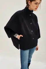 Tapado corto de paño en color azul marino, con cuello alto, cierre frontal de botones y mangas amplias de corte kimono. Presenta aberturas laterales en el ruedo y bolsillos frontales.