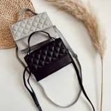 Cartera bandolera negra de ecocuero con diseño acolchado en rombos. Tiene asa corta superior y correa larga desmontable y regulable.