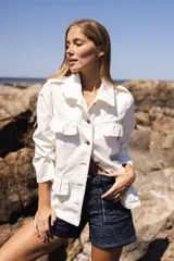 Chaqueta de denim liviana color blanco con volados en el frente, cuello camisero y cierre frontal de botones. Presenta un calce relajado y bolsillos funcionales.