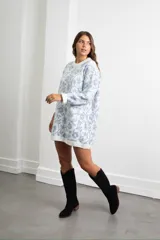 Vestido corto de tejido de punto con diseño oversize, cuello redondo y mangas largas con puños acanalados. Presenta un estampado floral en tonos blanco y celeste.