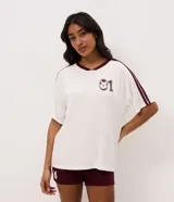 Pijama corto de dos piezas confeccionado en viscolycra. Incluye remera blanca de manga corta con cuello en V bordó, rayas en los hombros y estampa de Winnie The Pooh con el número 01 en el pecho, y short corto color bordó con cintura elastizada.