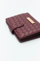 Billetera de mujer Daniel Cassin con diseño trenzado, cierre con broche a presión y placa metálica dorada con el logo de la marca en el frente.