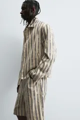 Cazadora de hombre de corte relajado, color beige claro con rayas verticales en azul oscuro con efecto desgastado o estampado. Presenta cuello solapa, manga larga, bolsillos de vivo en cadera y cierre frontal con botones a presión.