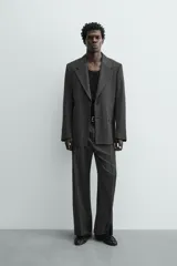 Blazer de corte regular fit en color gris oscuro, confeccionada en tejido con viscosa. Presenta cuello con solapas de muesca, cierre frontal con dos botones, bolsillos laterales con solapa y aberturas en la espalda.