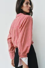 Camisa de cuello solapa y manga larga con rayas verticales rojas y blancas, con puños anchos blancos contrastantes y cierre frontal de botones.
