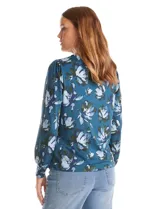 Blusa de seda fría con estampado floral en tonos verdes y azules. Presenta escote en V con un aplique metálico decorativo, mangas largas con puños y corte recto.